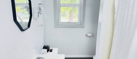 A bathroom with a white sink, a mirror, a window, and a shower curtain.