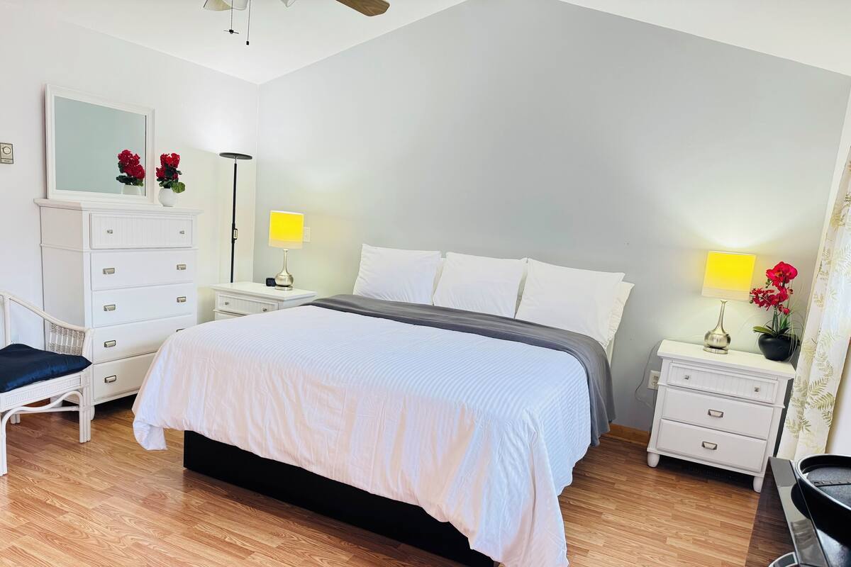 A neatly arranged bedroom with a bed, bedside tables, a dresser, a chair, and a mirror.