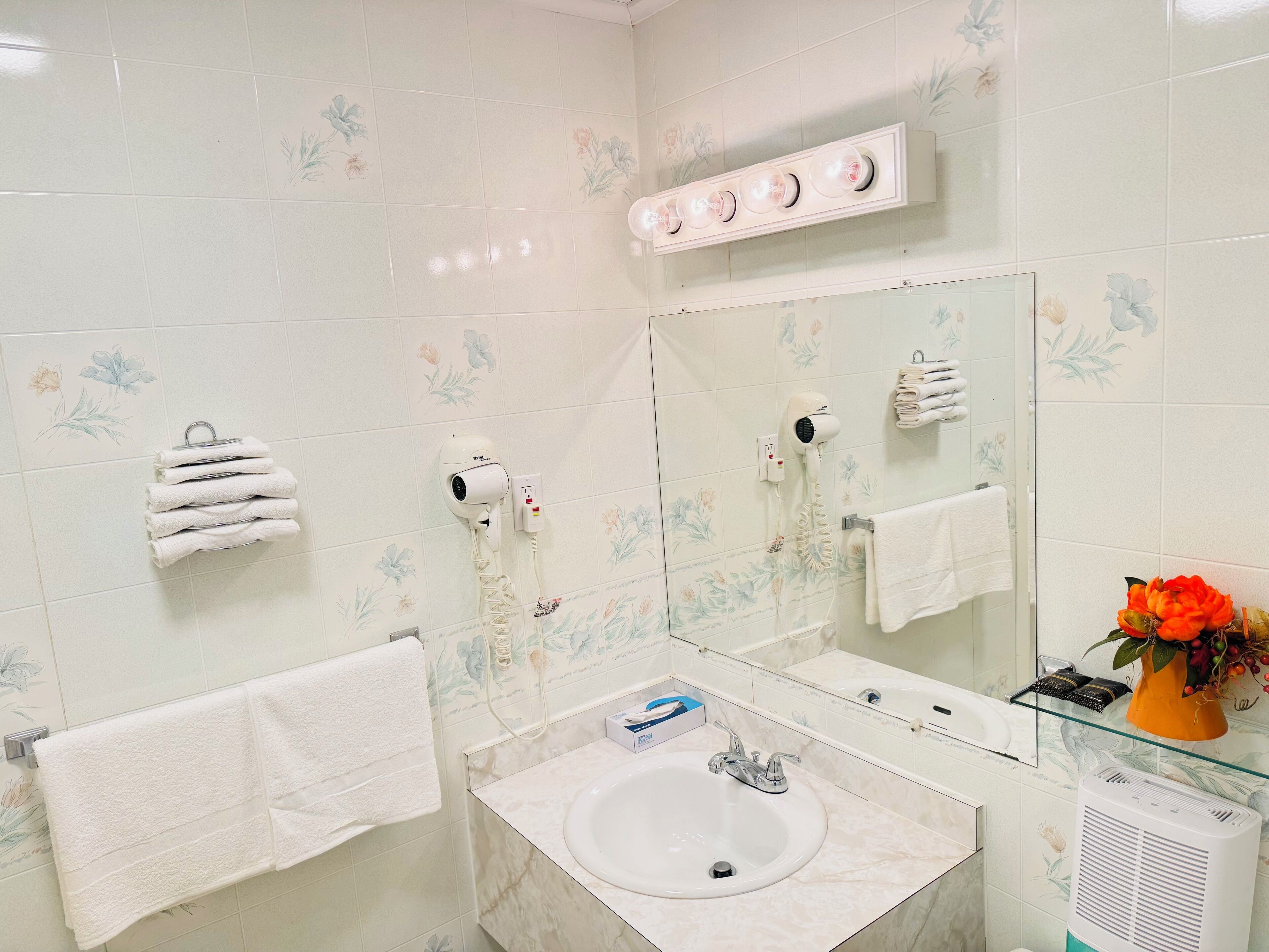 Un baño con un lavamanos blanco, un espejo y dos secadores de pelo fijados a la pared.