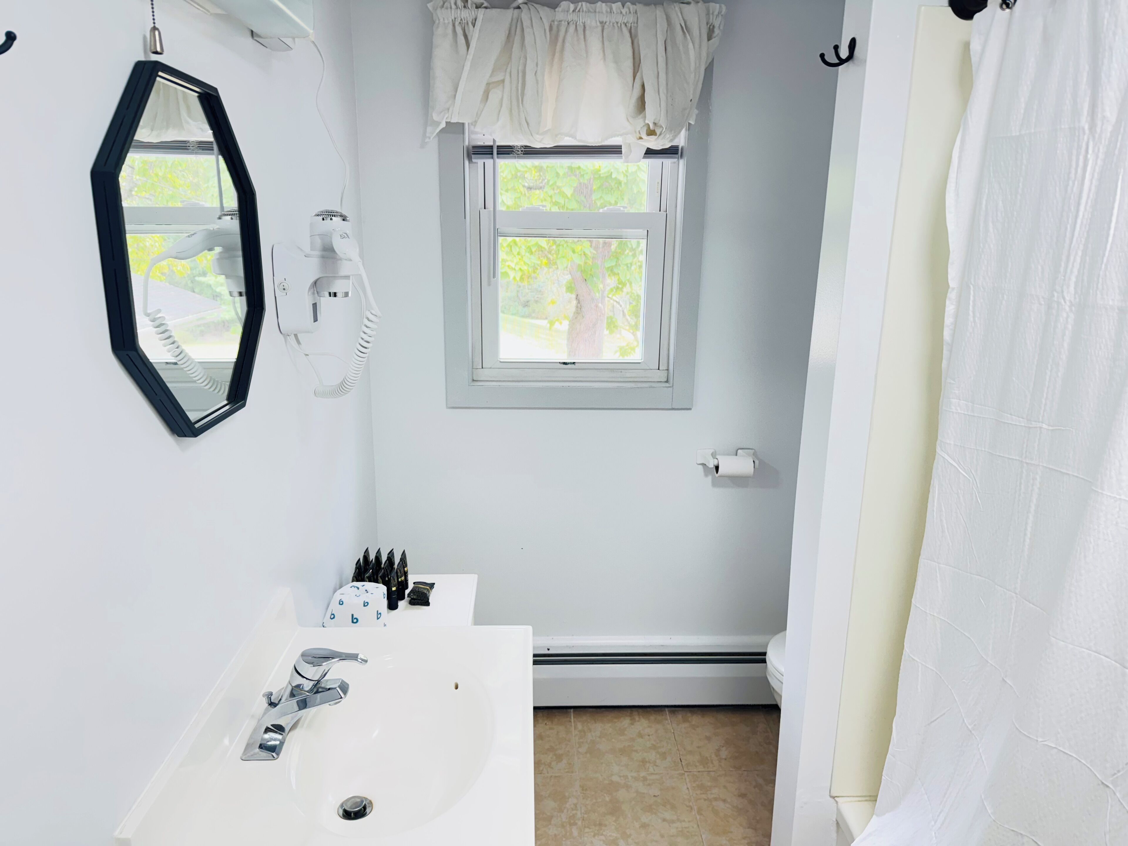 A bathroom with a white sink, a mirror, a window, and a shower curtain.