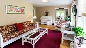 A living room with a floral sofa, a white coffee table, a white piano, and a wicker chair. - Pocono Ridge Inn (East Stroudsburg)
