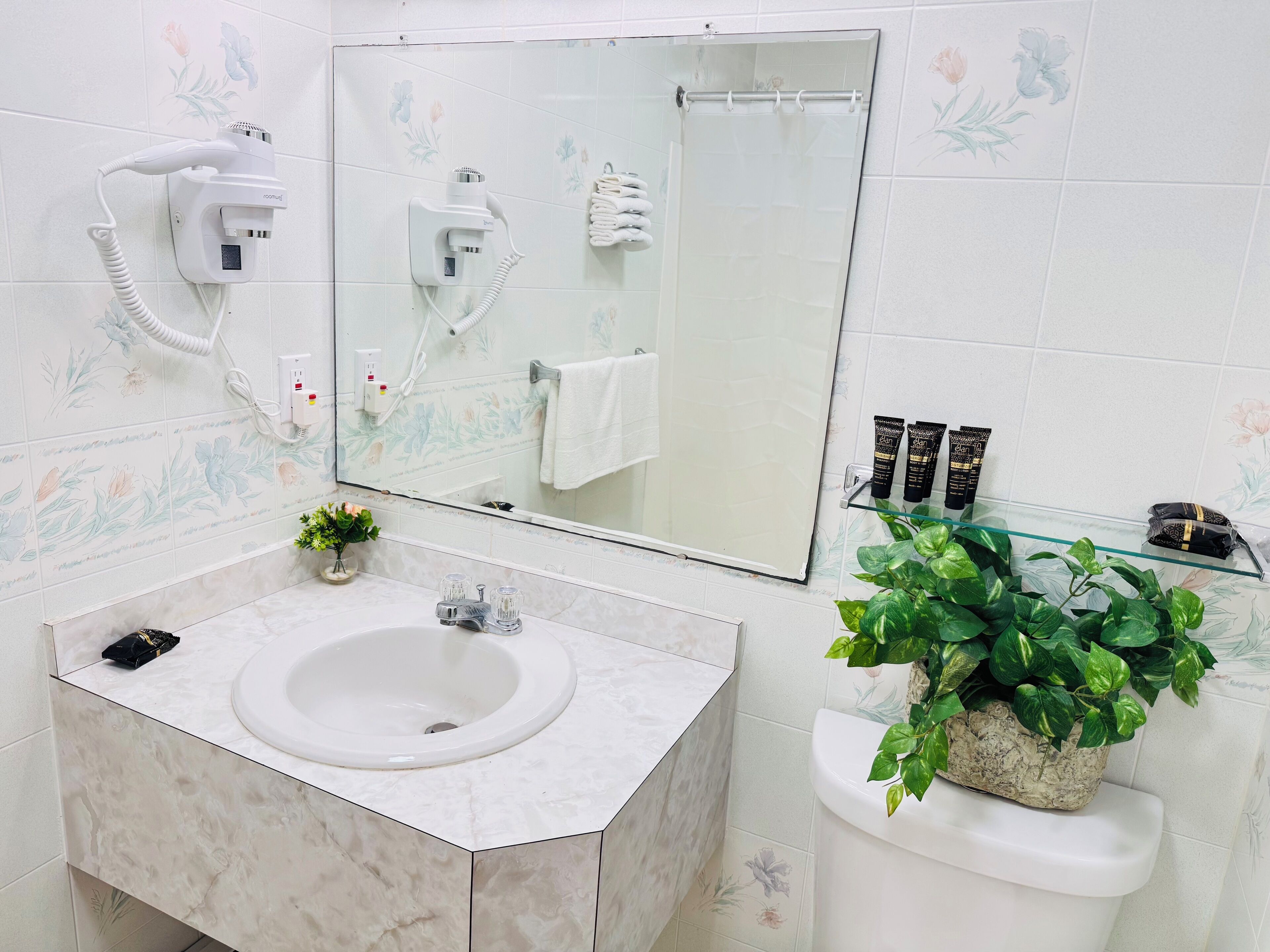 A bathroom with a white sink, a mirror, a hairdryer, a towel rack, and a potted plant.