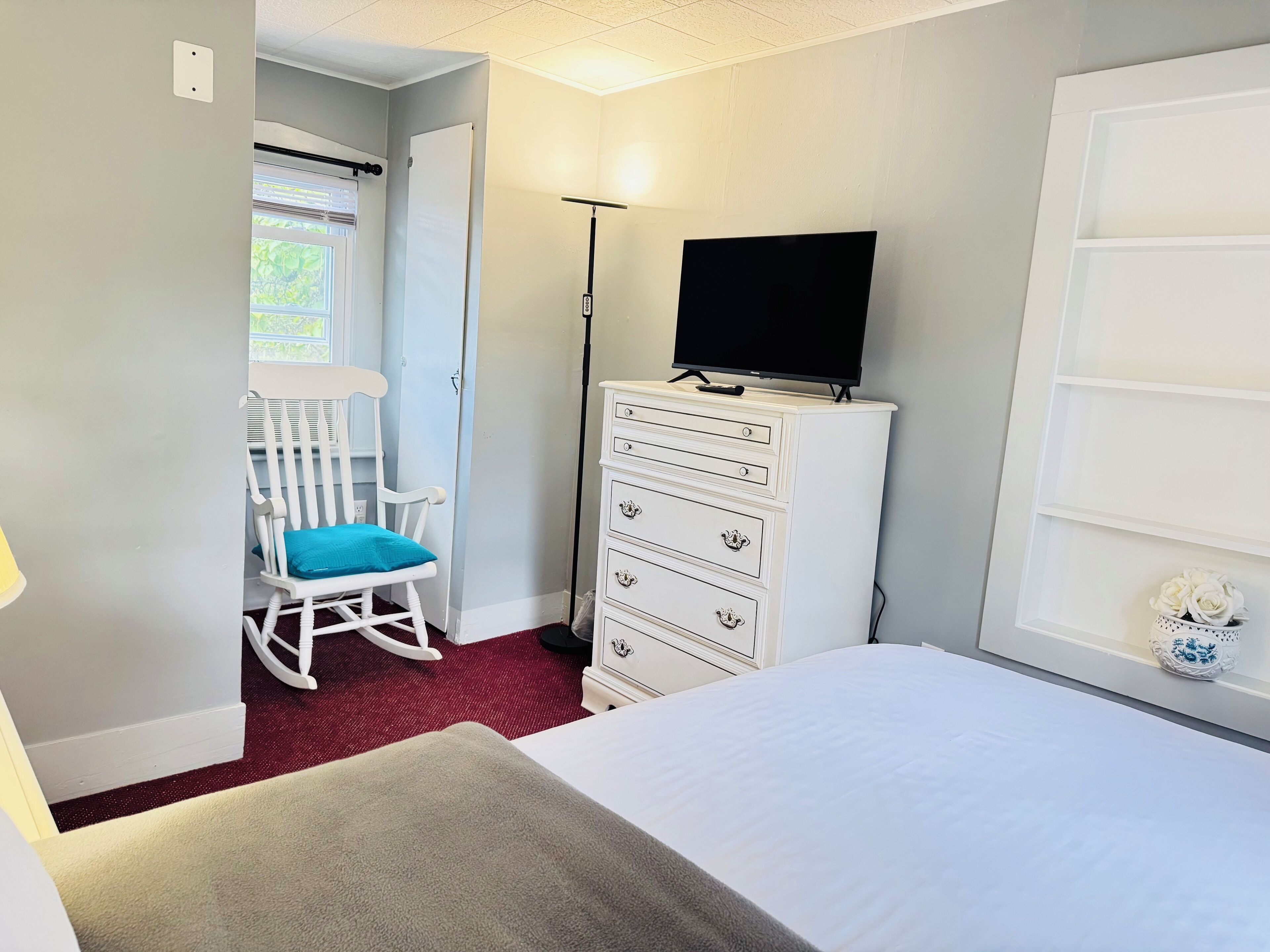 Une chambre à coucher avec un lit, une commode, un fauteuil à bascule et un téléviseur.