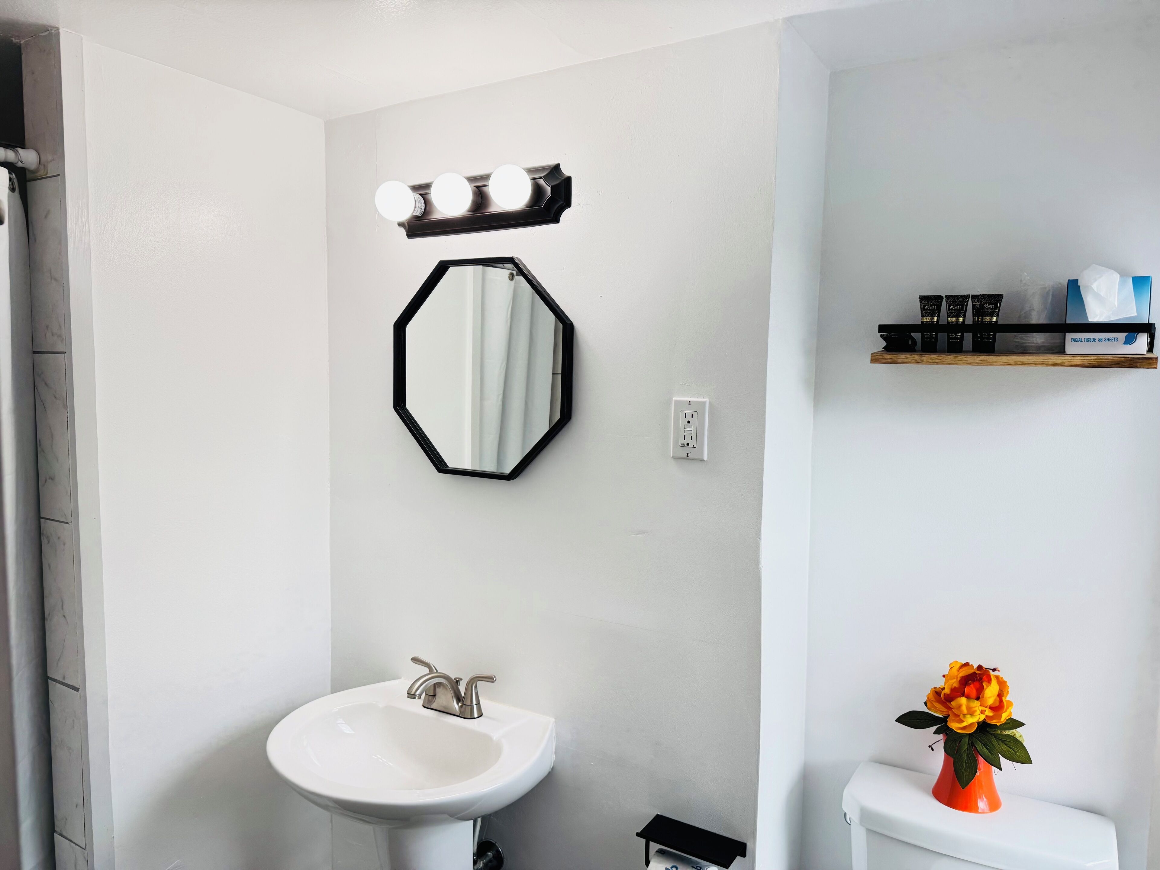 Un baño con lavamanos blanco, un espejo y repisas con artículos de tocador.
