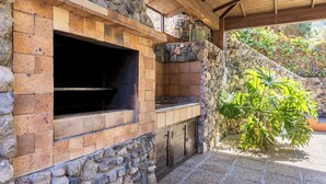Un four en briques installé à l’extérieur, avec des murs en pierre et un toit en bois, le tout entouré de verdure.