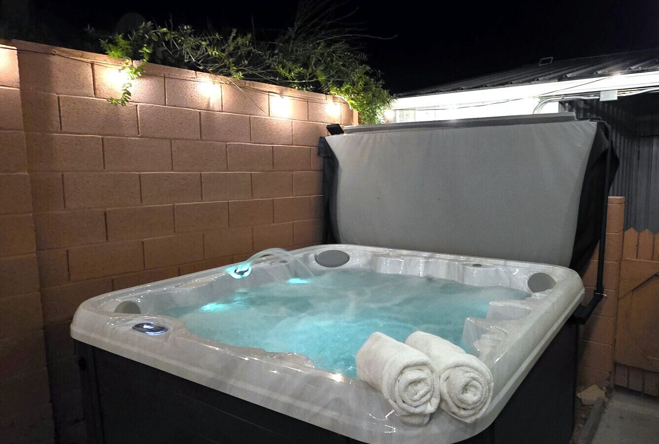 Un bain à remous doté d’un couvercle transparent, une serviette enroulée et un mur de briques en arrière-plan.