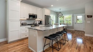 Une cuisine moderne avec des meubles blancs, un grand îlot central doté de tabourets, des appareils en acier inoxydable et un lustre.
