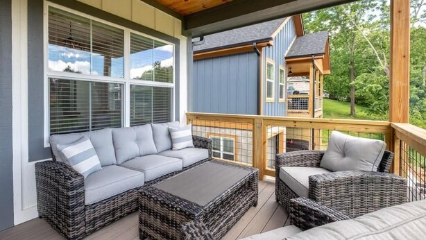 Une terrasse extérieure couverte, aménagée avec des meubles en osier, notamment un canapé et des fauteuils, et dotée d’une rambarde en bois.