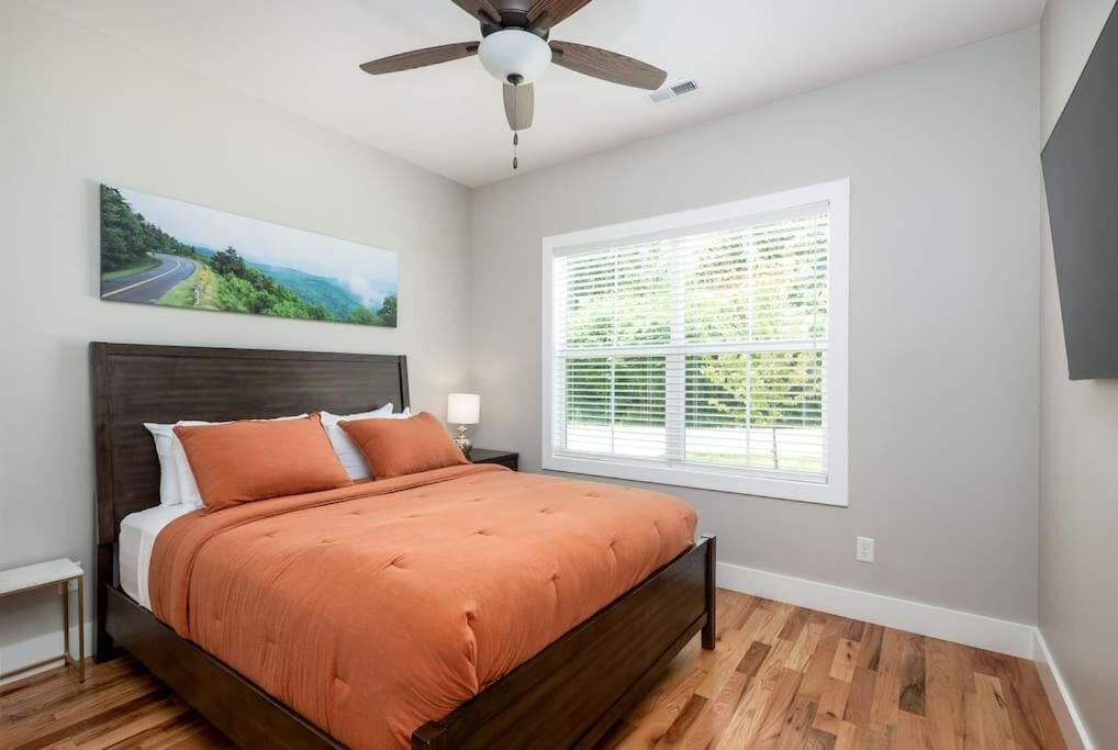 A bedroom with a wooden bed, a ceiling fan, a window with blinds, and a painting on the wall.