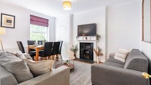 Una sala de estar moderna con chimenea, un comedor con mesa y sillas, y un televisor grande montado en la pared.