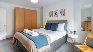 Un dormitorio moderno con una cama grande, un armario de madera, mesitas de noche y un espejo.