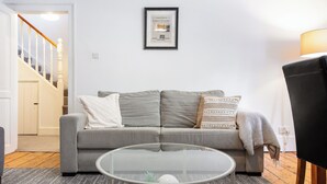 Un salón con un sofá gris, una mesa de centro de vidrio y un cuadro enmarcado en la pared.