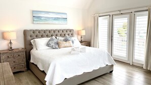A bedroom with a large bed, two bedside tables, a headboard, a painting on the wall, and a view through the window. - Gulf Dreamin' - Waterfront, Destin Harbor, Private Dock, 2 Kings, New to VRBO! (Destin)