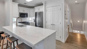 A modern kitchen with white cabinetry, a stainless steel refrigerator, a built-in microwave, and a marble island with bar stools. - Gulf Dreamin' - Waterfront, Destin Harbor, Private Dock, 2 Kings, New to VRBO! (Destin)