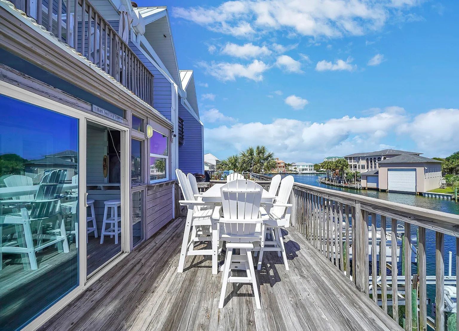 A wooden deck with a table and chairs, overlooking a body of water and a marina.
