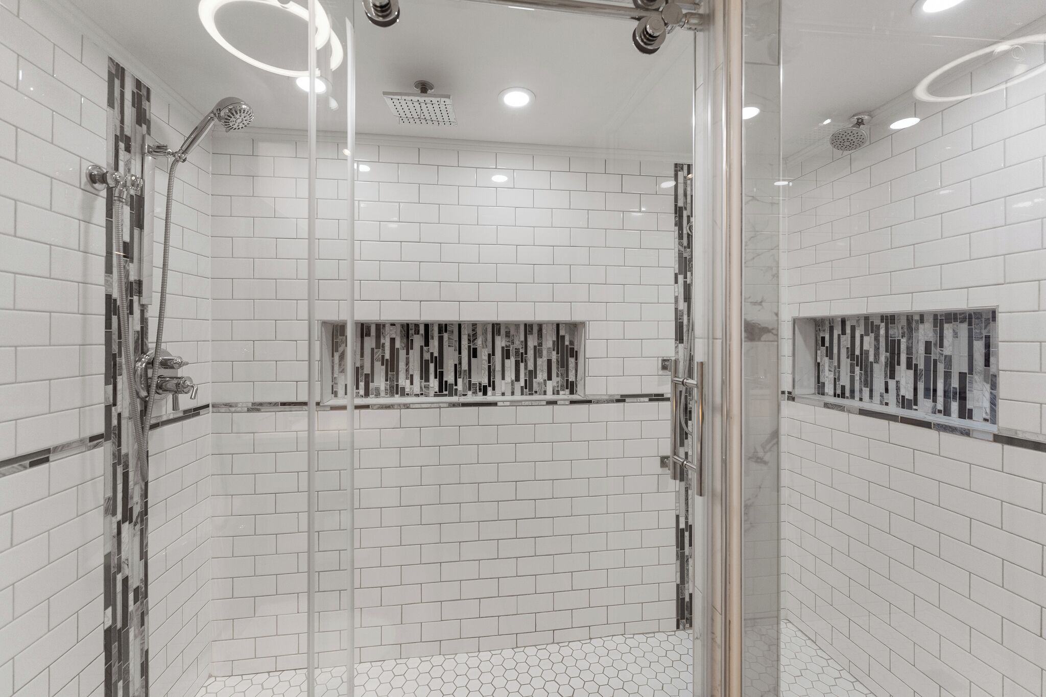 A modern shower with a glass door, white tiled walls, and a unique patterned tile accent.