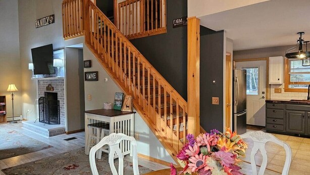 A spacious living room with a wooden staircase, a fireplace, and a dining area with a floral centerpiece.
