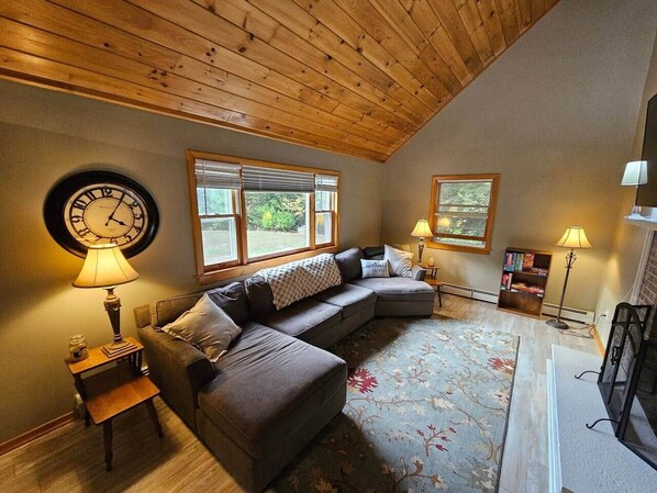 Una sala de estar acogedora con un sofá modular, un reloj de pared redondo y dos ventanas con persianas.