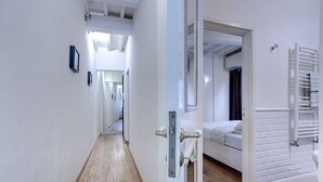 Un corridoio che porta a una camera da letto con un letto, un termosifone e una porta con maniglia.