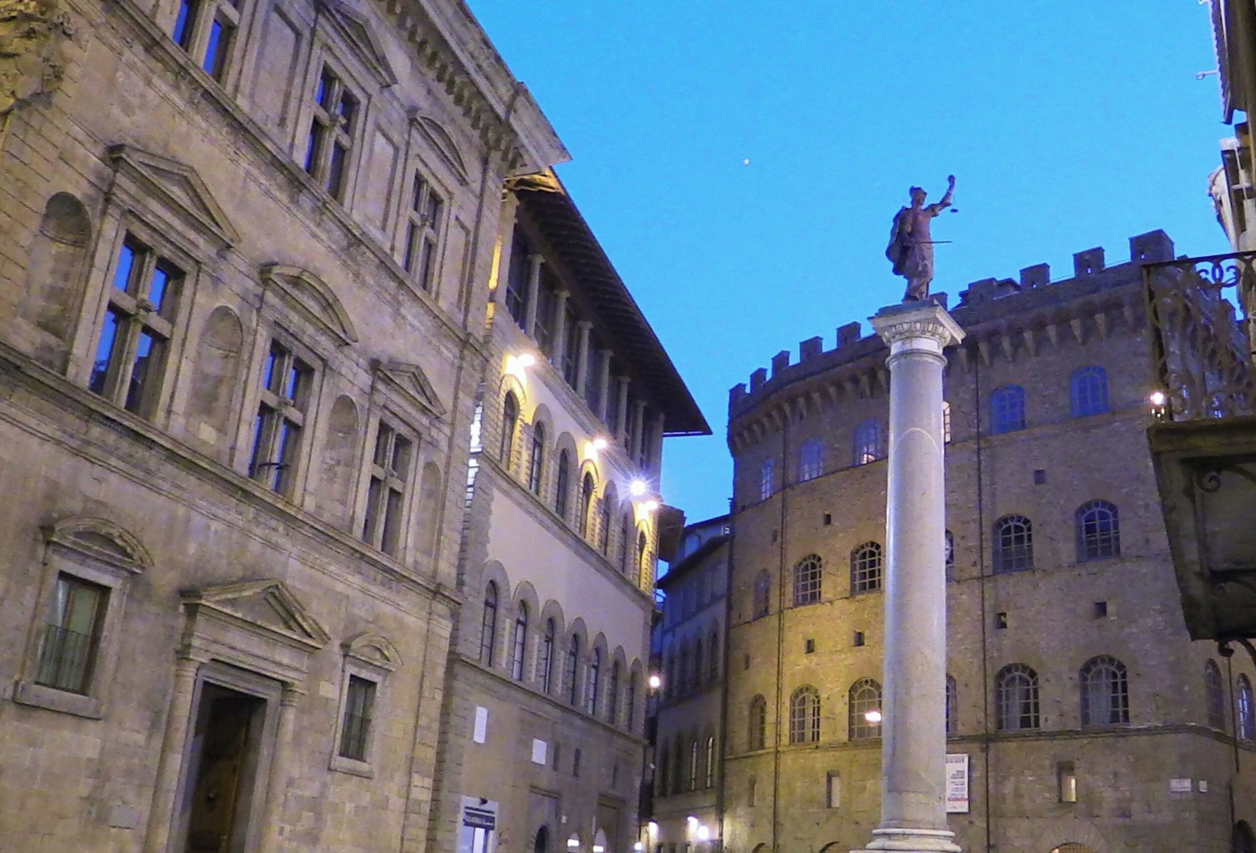 A historic building with classical architecture, featuring arched windows and a central column with a statue.