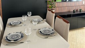 Un comedor con una mesa dispuesta para dos personas, un televisor montado en la pared y una planta en maceta sobre una estantería.