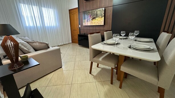 Una sala de estar moderna con un sofá, una mesa de comedor para cuatro personas y un televisor montado en la pared.