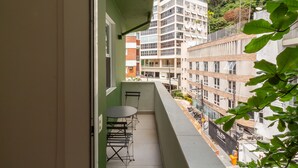 Ein Balkon mit Tisch und Stühlen, mit Blick auf eine Stadtlandschaft mit Gebäuden und einer Anhöhe.