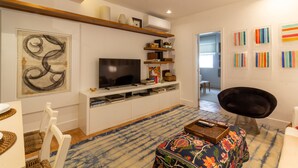Ein modernes Wohnzimmer mit Flachbildfernseher, weißen Regalen, einem gemusterten Teppich und einem schwarzen Sessel.