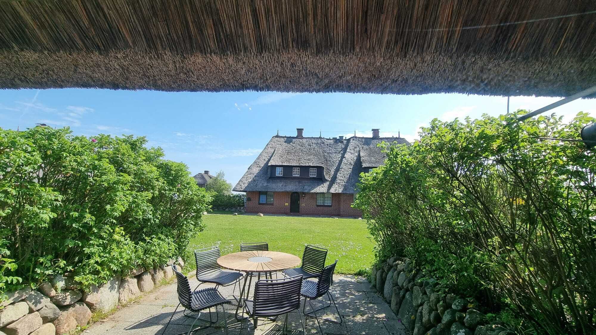 A thatched-roof house with a lawn and a round table with chairs in the foreground.