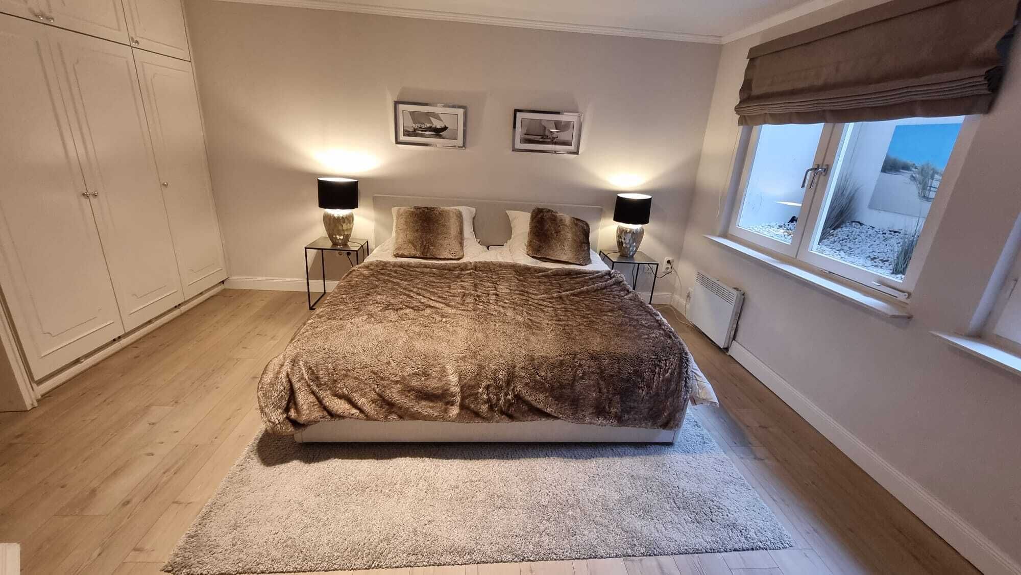 Une chambre à coucher avec un grand lit, deux lampes de chevet, une fenêtre donnant sur un beau paysage et un radiateur.