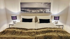 Ein Bett mit Felldecke, zwei Nachttischlampen, ein Vorhang mit einem Bild und ein kleiner Tisch neben dem Bett.
