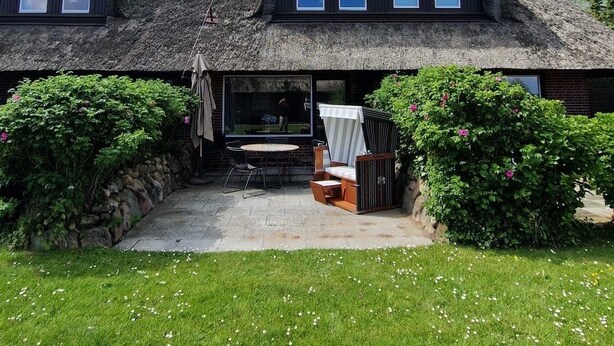 Ein reetgedecktes Haus mit vielen Fenstern und einer Terrassenfläche.
