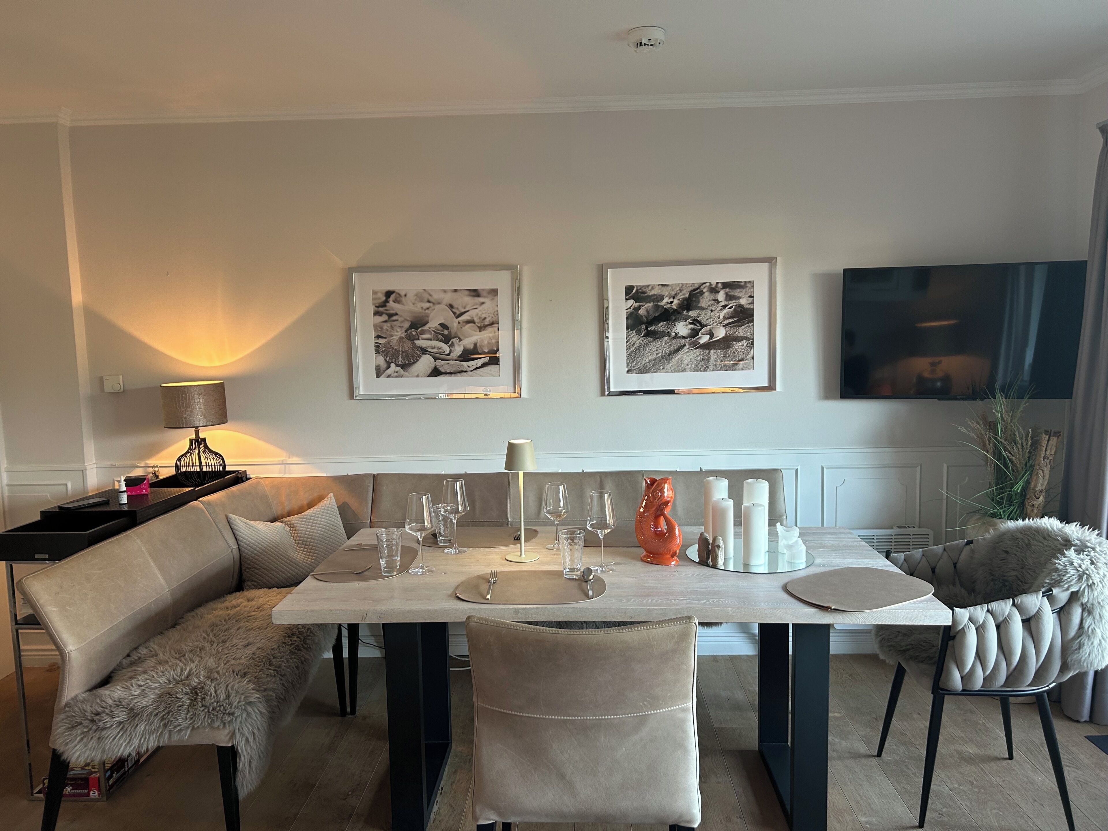Un coin repas avec une table dressée pour quatre personnes, un canapé et deux tableaux encadrés au mur.