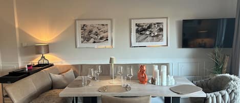 Un coin repas avec une table dressée pour quatre personnes, un canapé et deux tableaux encadrés au mur.