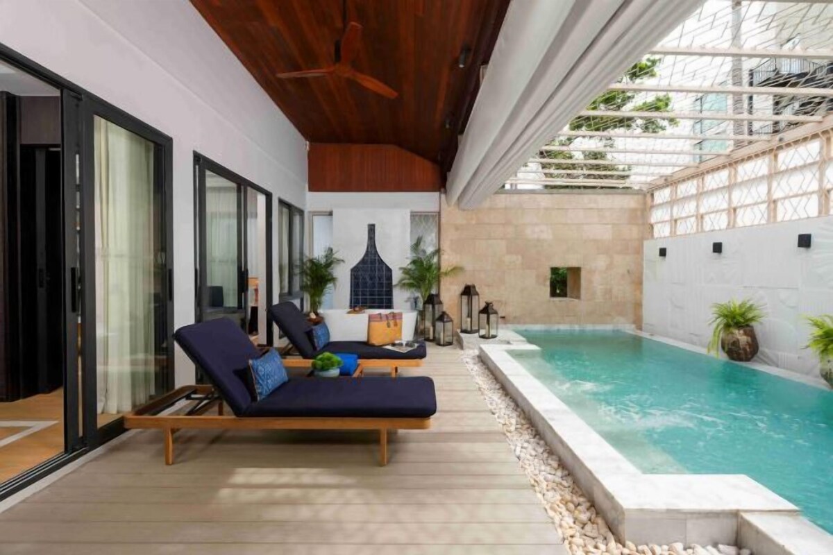 A poolside area with lounge chairs, a small table, and potted plants.