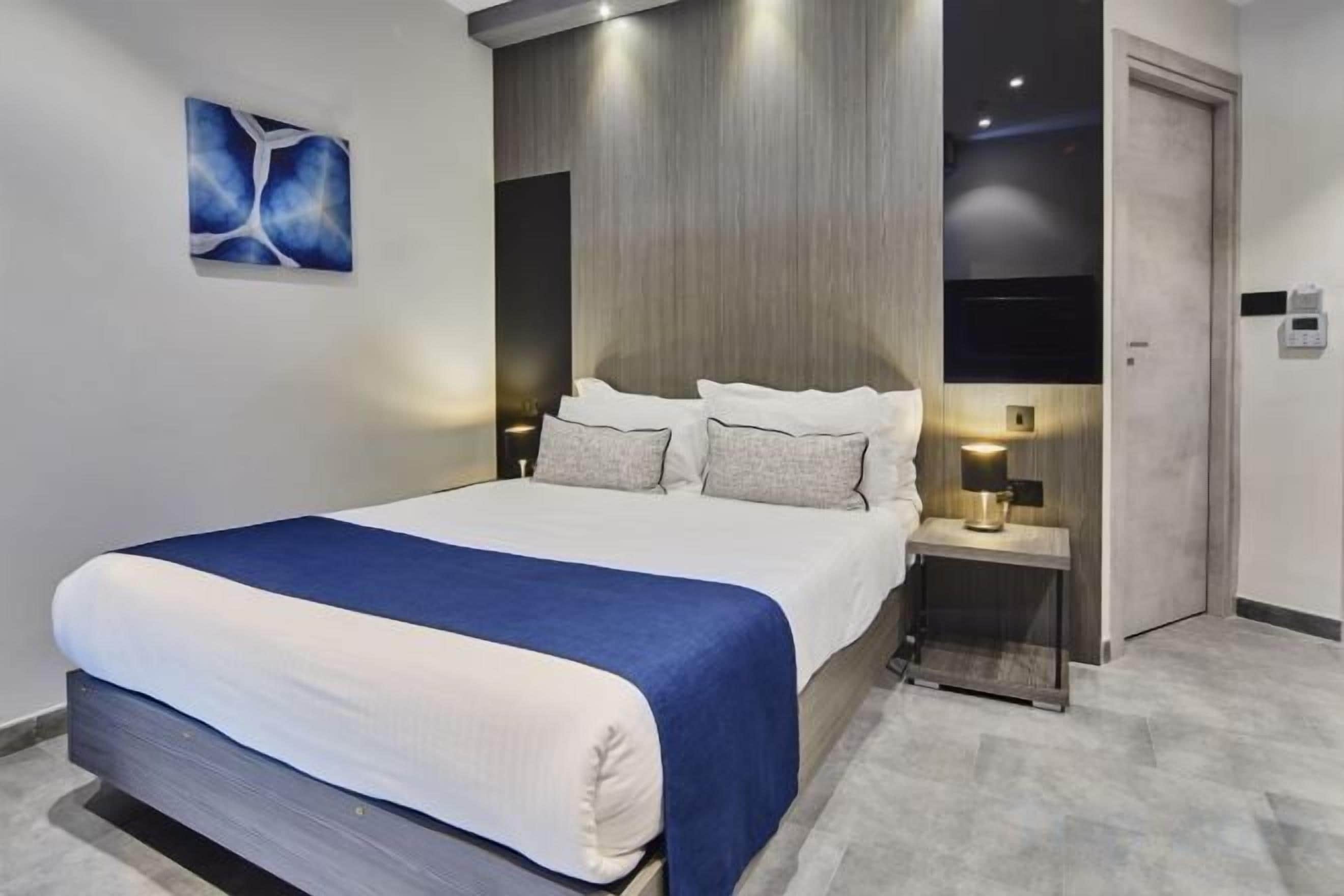 Ein modernes Hotelzimmer mit einem großen Bett, Nachttischlampen, einem kleinen Tisch und einer Tür.