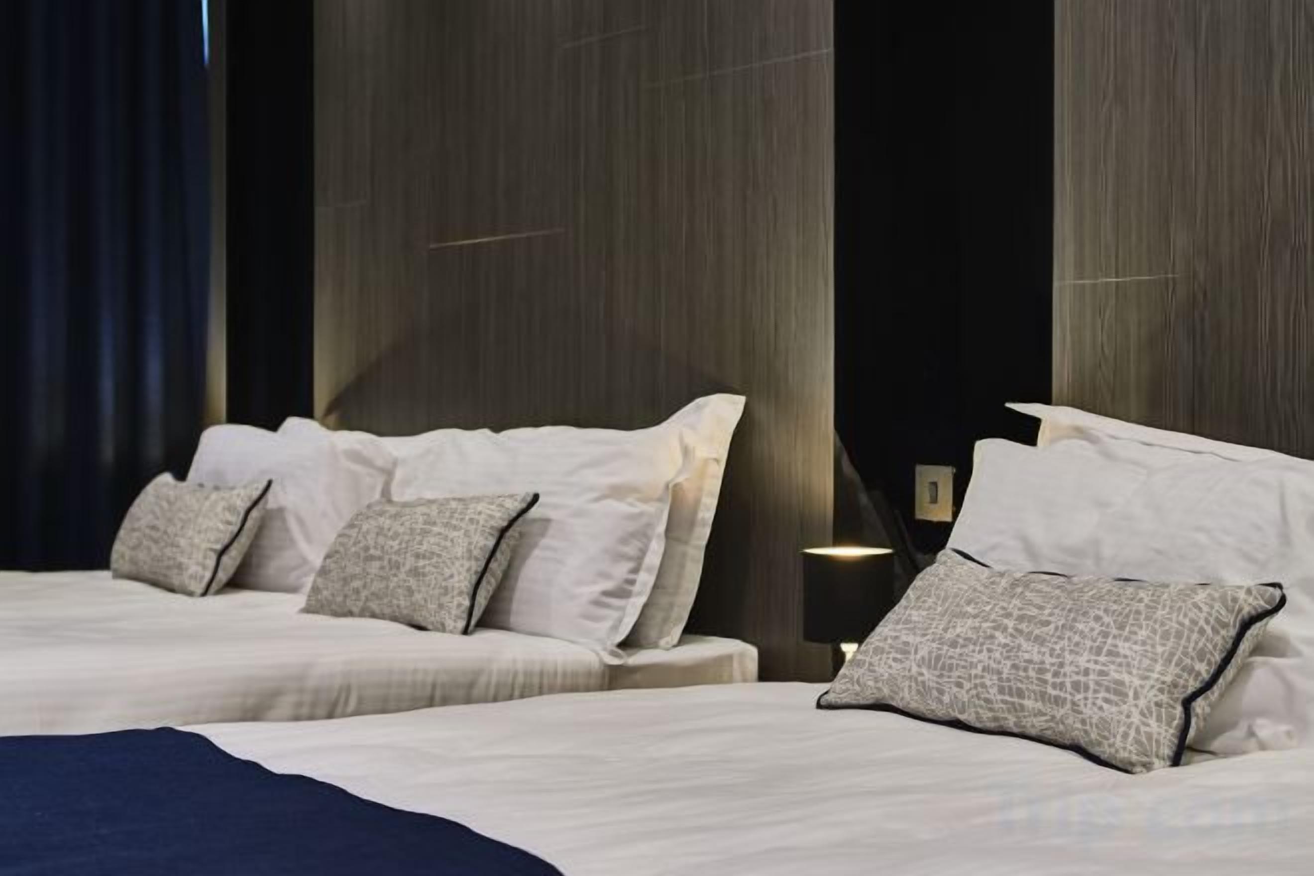 Una camera d'albergo con due letti, una tenda scura e un muro con linee verticali.