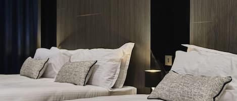 Habitación de hotel con dos camas, una cortina oscura y una pared con líneas verticales.