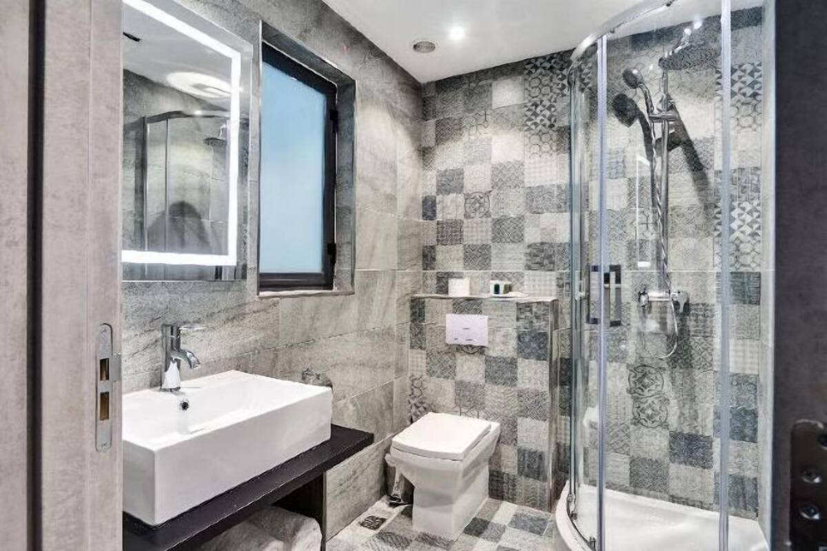 A modern bathroom with a large mirror, a white sink, a toilet, and a glass-enclosed shower area.