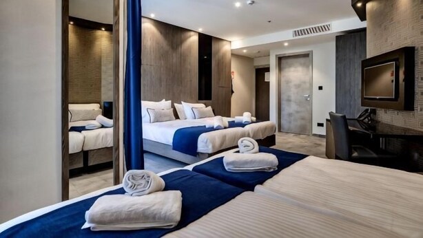A hotel room with two beds, a TV, a mirror, and a desk. - The District Hotel (Swieqi)