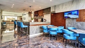 A modern bar area with marble flooring, blue bar stools, and a flat-screen TV mounted on the wall. - The District Hotel (Swieqi)