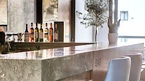 A modern bar area with a marble countertop, several bottles of alcohol, and a potted plant. - The District Hotel (Swieqi)