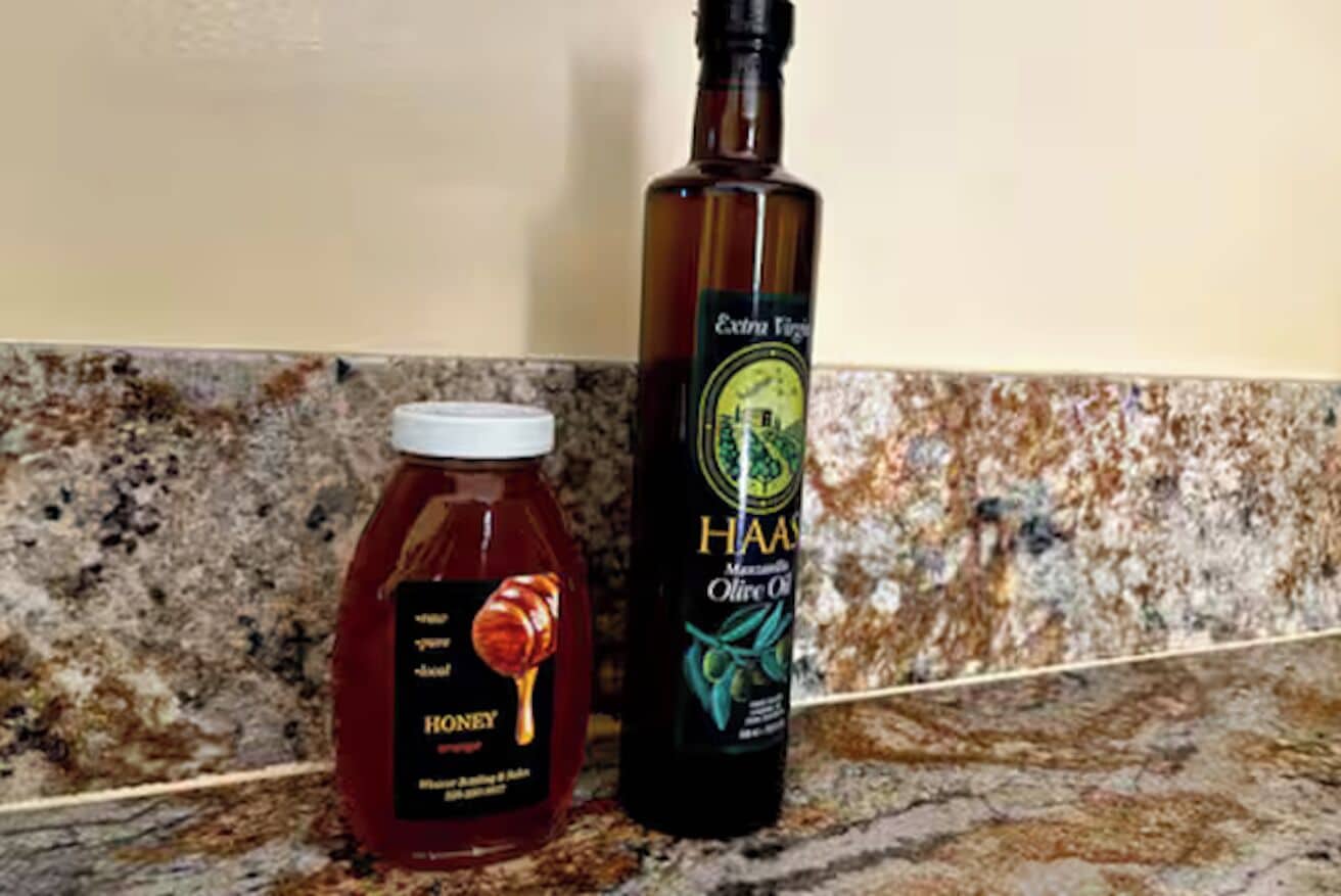 A jar of honey and a bottle of extra virgin olive oil on a granite countertop.
