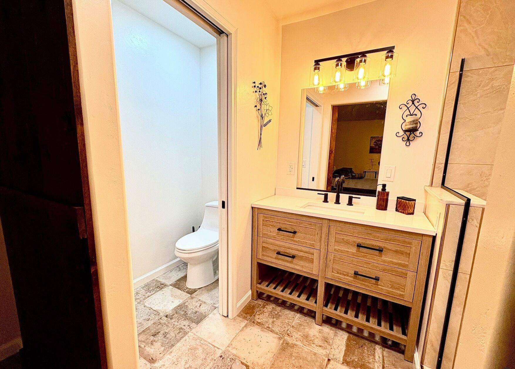 A bathroom with a white toilet, wooden vanity with drawers, a mirror, and a light fixture above the mirror.