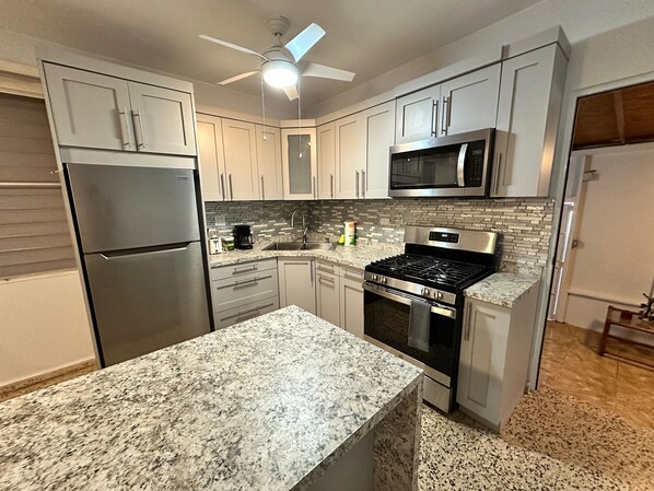 A modern kitchen with granite countertops, stainless steel appliances, and a ceiling fan.