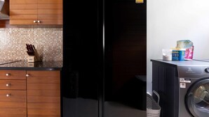 A kitchen with a black refrigerator, a washing machine, and wooden cabinets. - The Villa In The Sky: Luxurious Abundance, Breathtaking Views, Premier Comfort (Kathu)