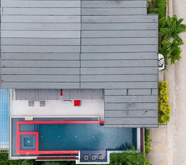 An aerial view of a building with a swimming pool, a covered patio area, and a small garden with palm trees.