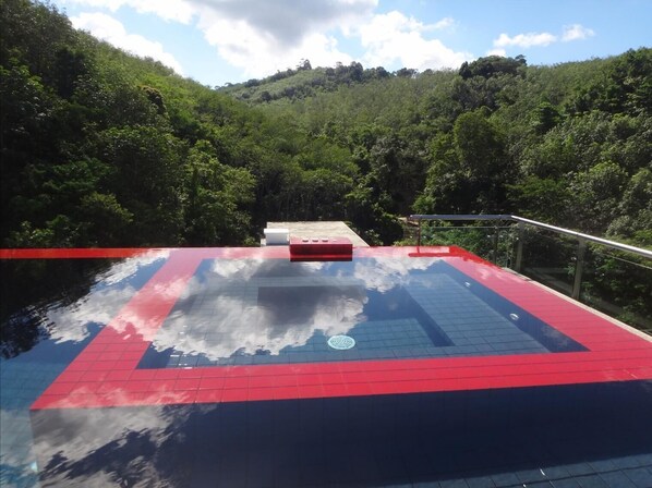 A rooftop pool with red and blue tiles, surrounded by lush greenery and hills.