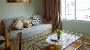 A living room with a sofa, a glass coffee table with a plant, and a painting on the wall. - Flats Aconchegantes (Campos do Jordão)