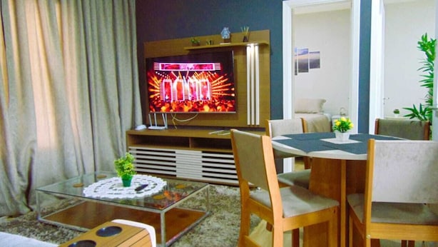 A living room with a television, a dining table, chairs, a coffee table, and a sofa. - Flats Aconchegantes (Campos do Jordão)